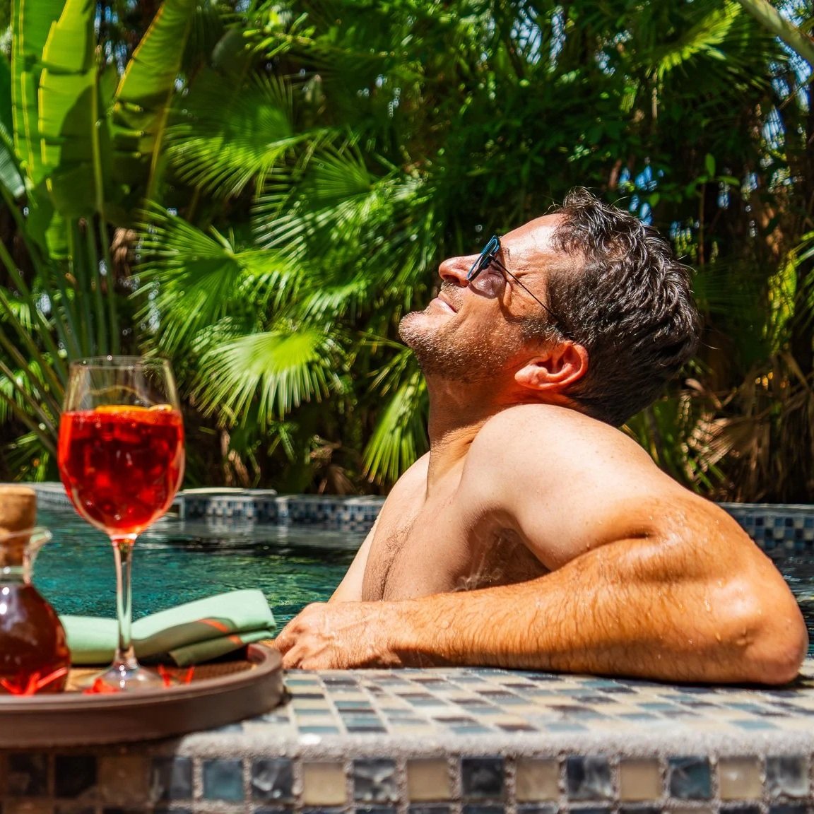 A man holding a woman up in the air outdoors, with a mountain range and cloudy sky in the background.