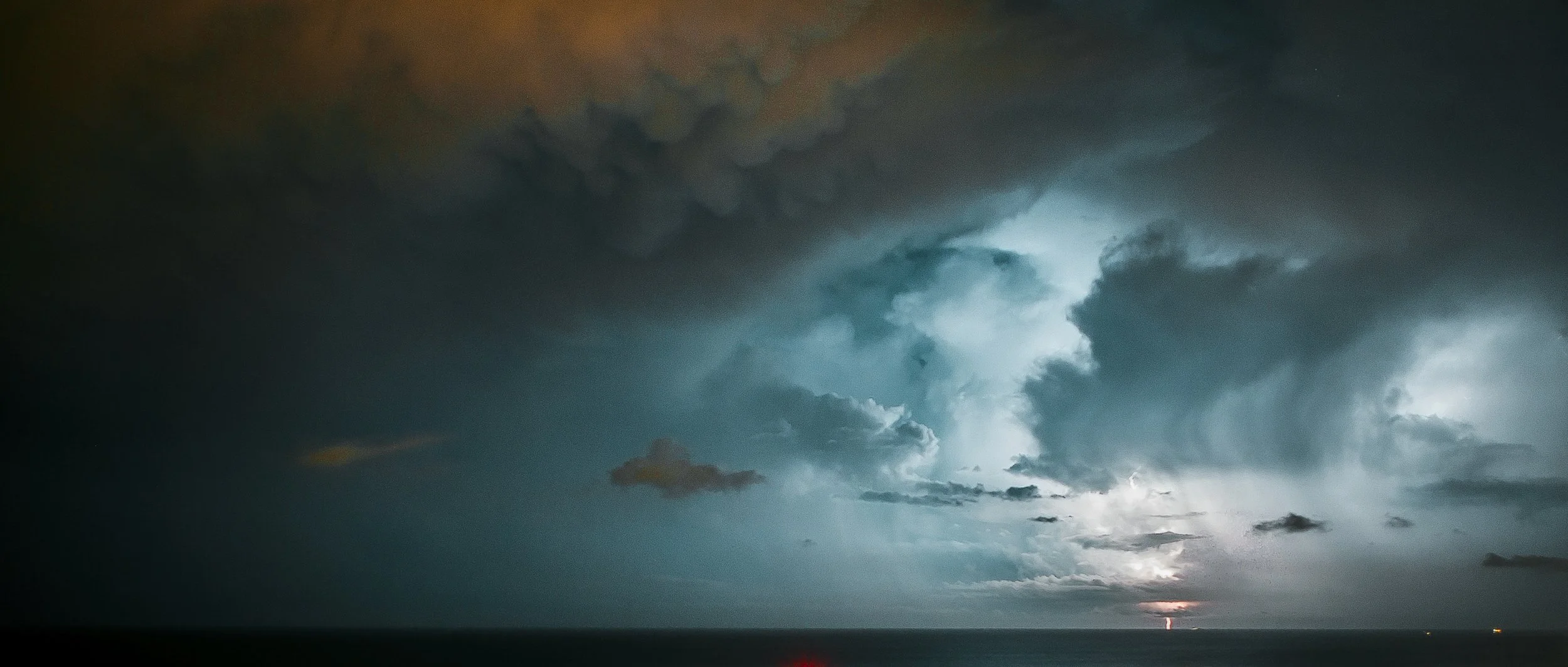 Dark cloudy sky over the ocean with lightning illuminating the clouds.