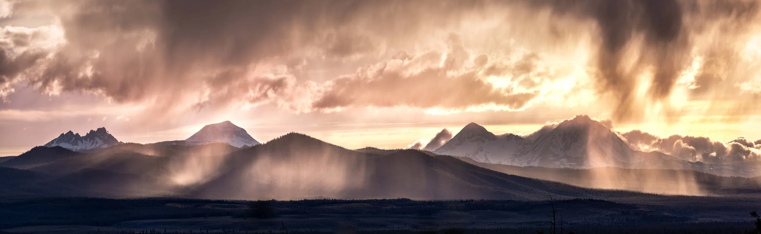 Snow-capped mountain range with dramatic clouds and sunbeams, creating a misty atmosphere.