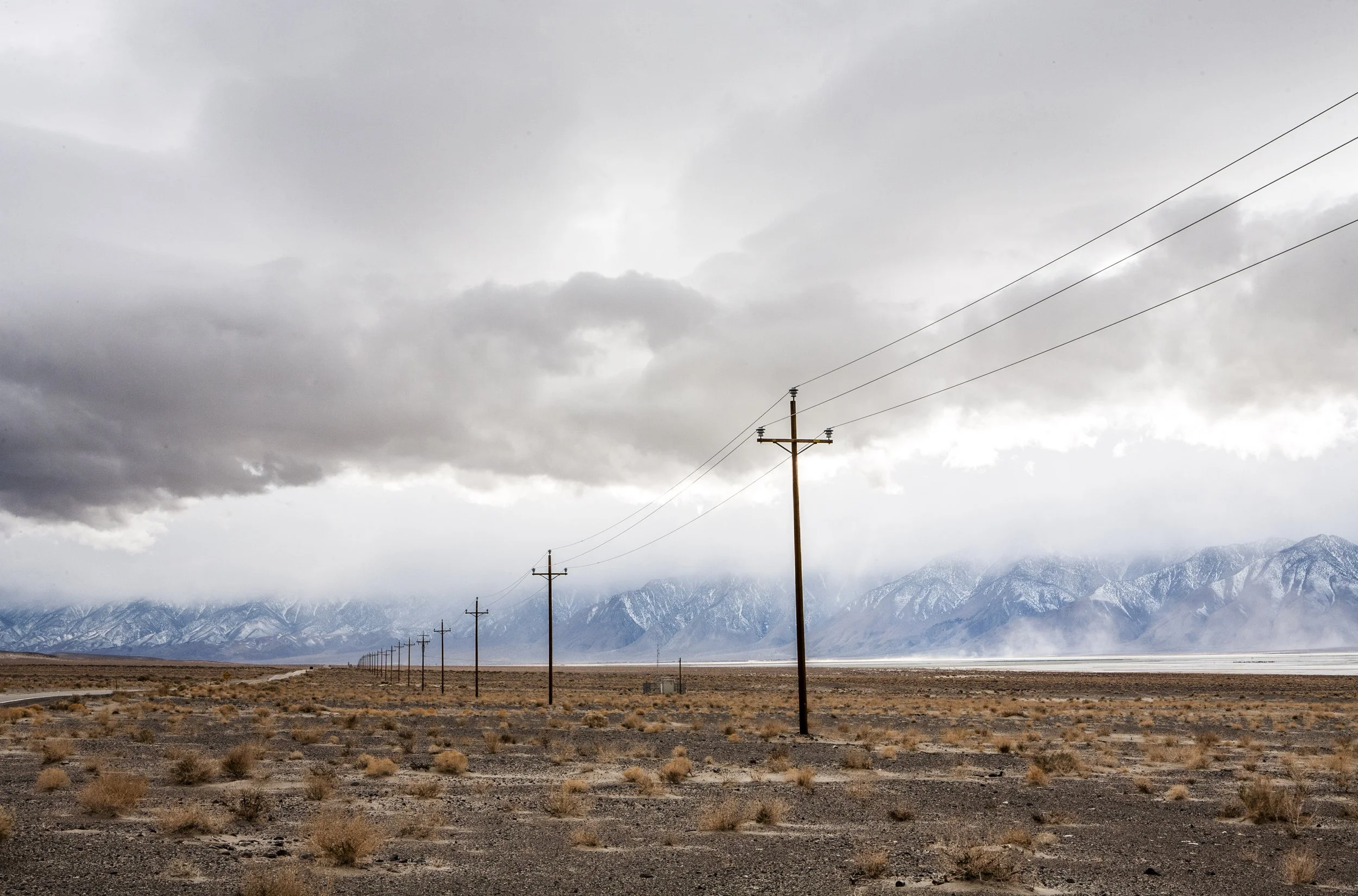 Desert landscape with utility poles, distant mountains, and cloudy sky.