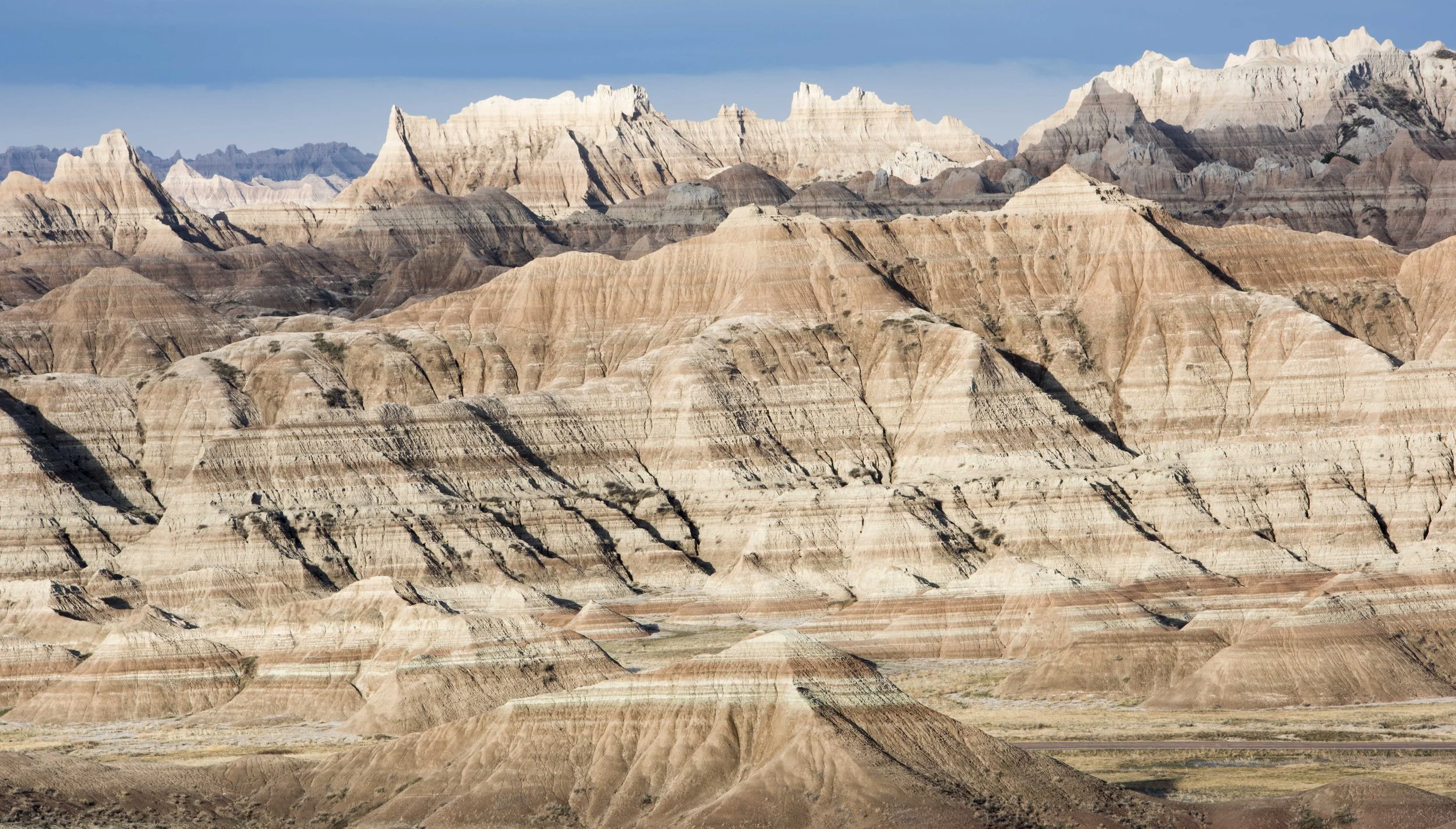 Eroded rock formations in Badlands National Park, featuring layered sedimentary rock and rugged, striated peaks under a clear sky.