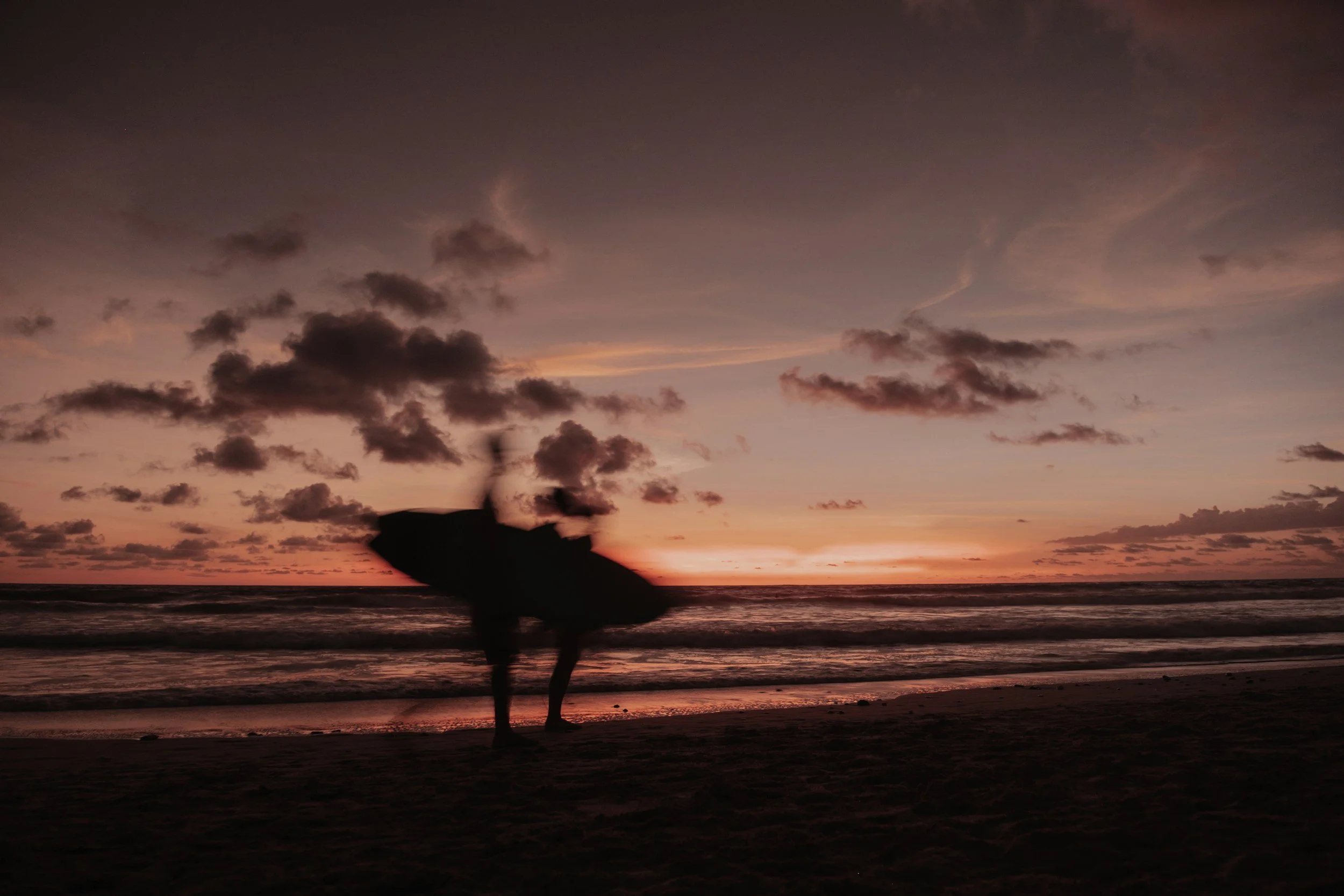Group of people riding horseback along a sandy beach with trees in the background and ocean waves on the right.