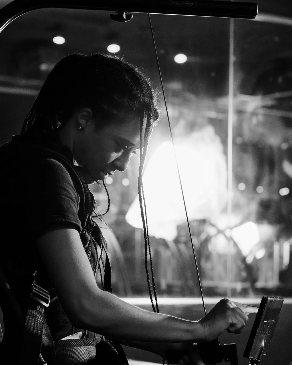 A woman with dreadlocks looking at her phone in a dimly lit environment, with a bright light source behind her.
