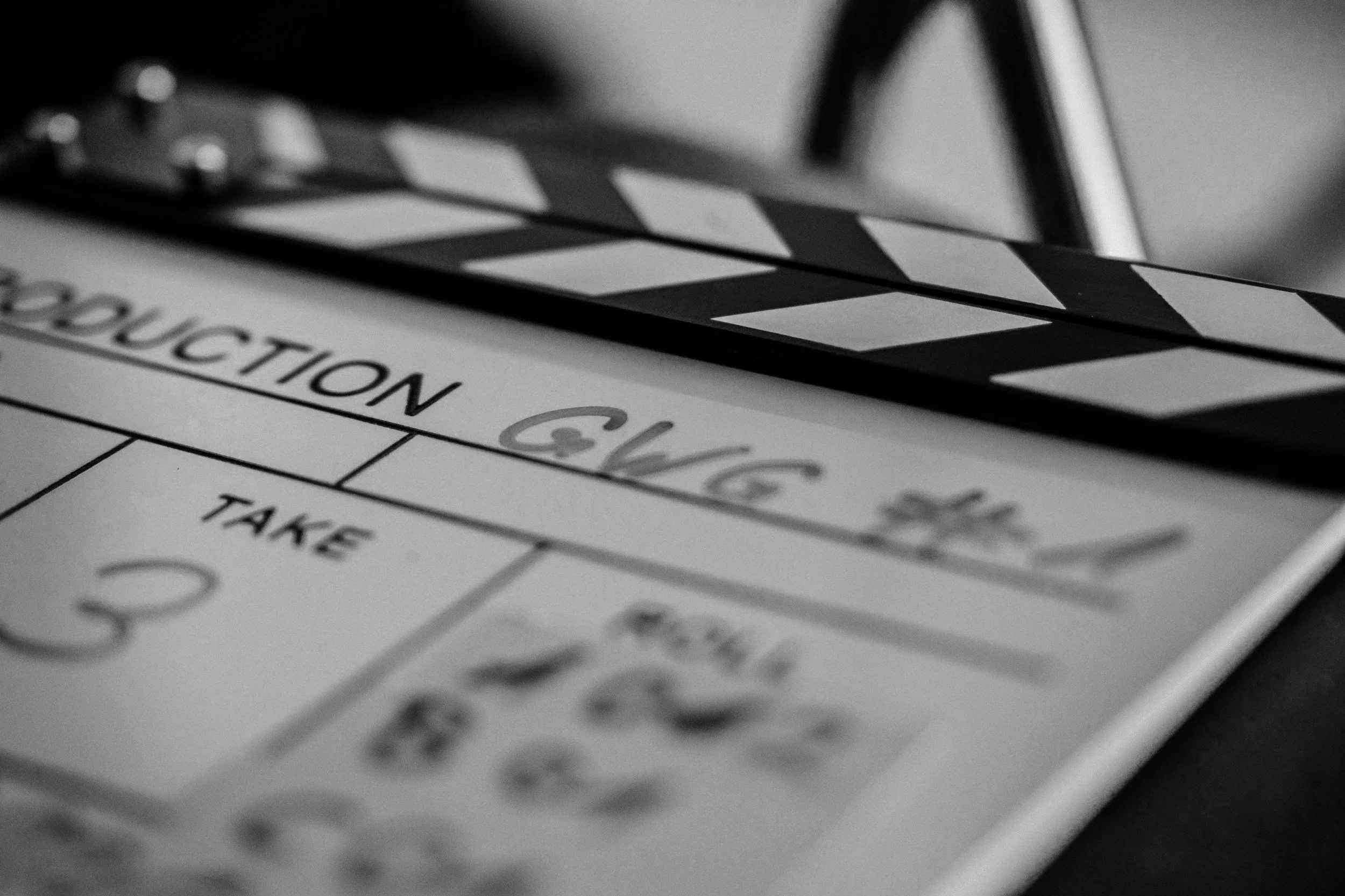 Close-up of a film clapperboard resting on a script or production schedule with the word 'PRODUCTION' visible, in black and white.