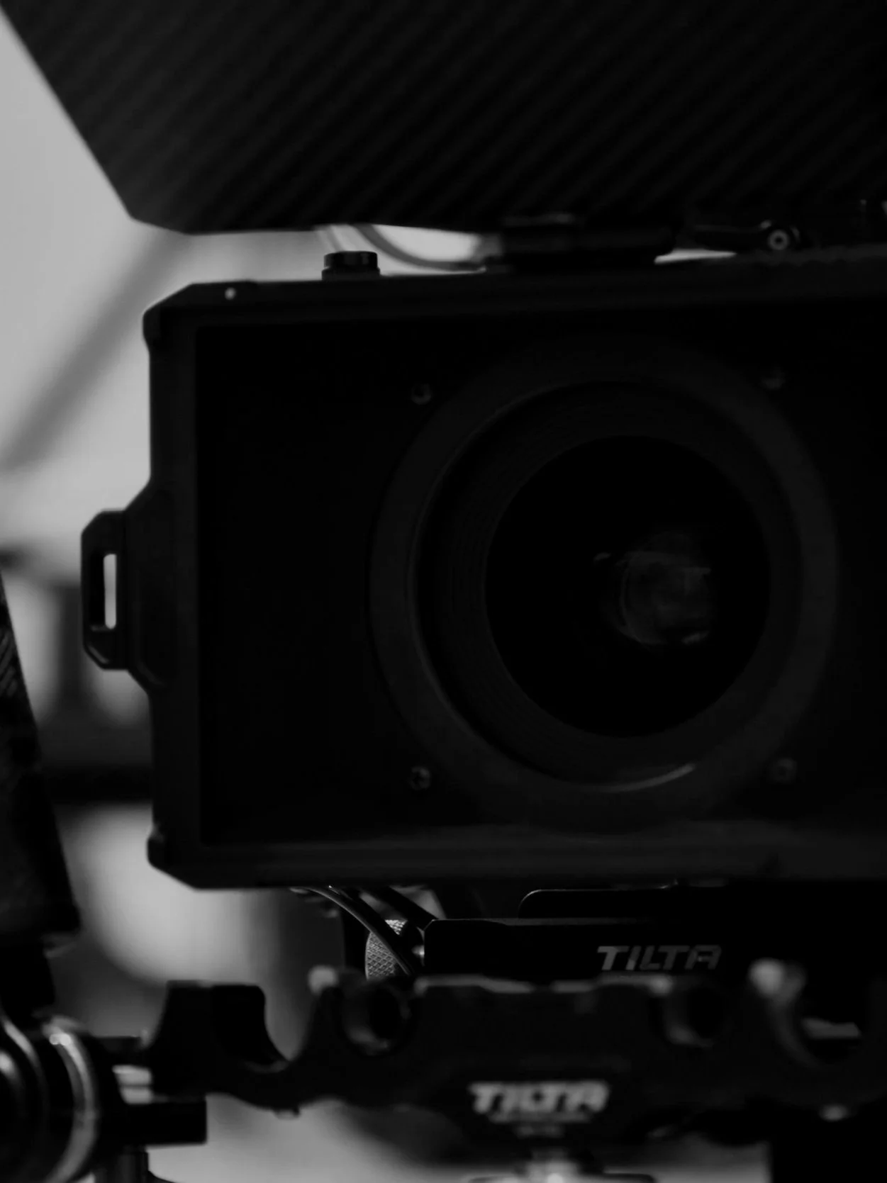 Black camera with a large lens mounted on a stabilizer or mount, with cables and a dark textured surface in the background.