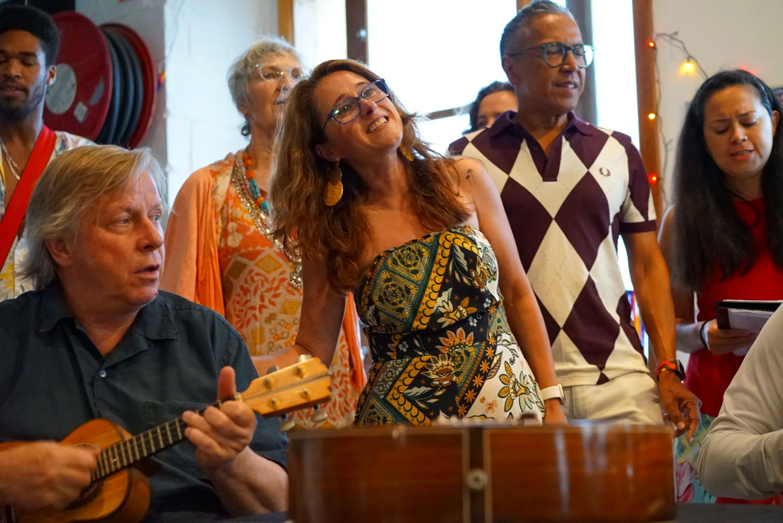 Group of people singing and playing guitar indoors, with colorful clothing and decor.
