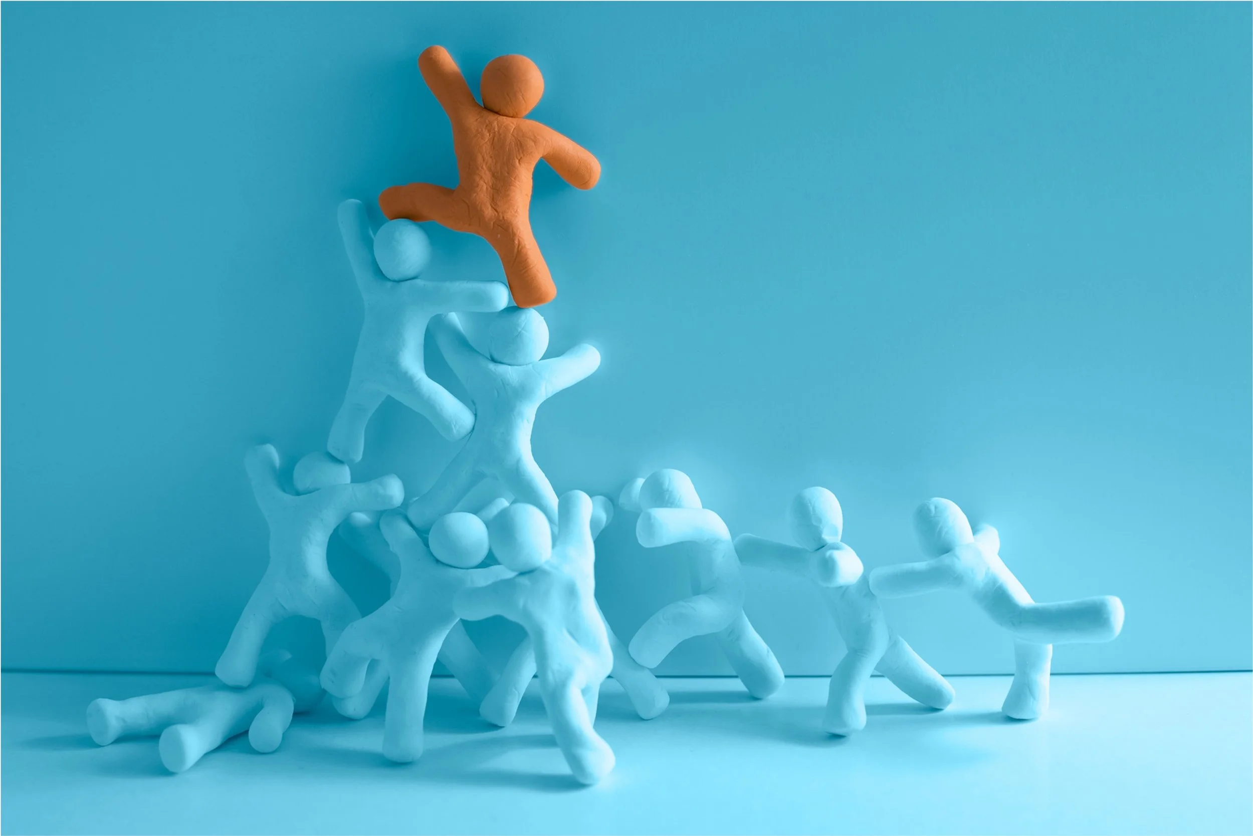 Multiple light blue and one orange clay figure in various poses stacked on top of each other against a light blue background.