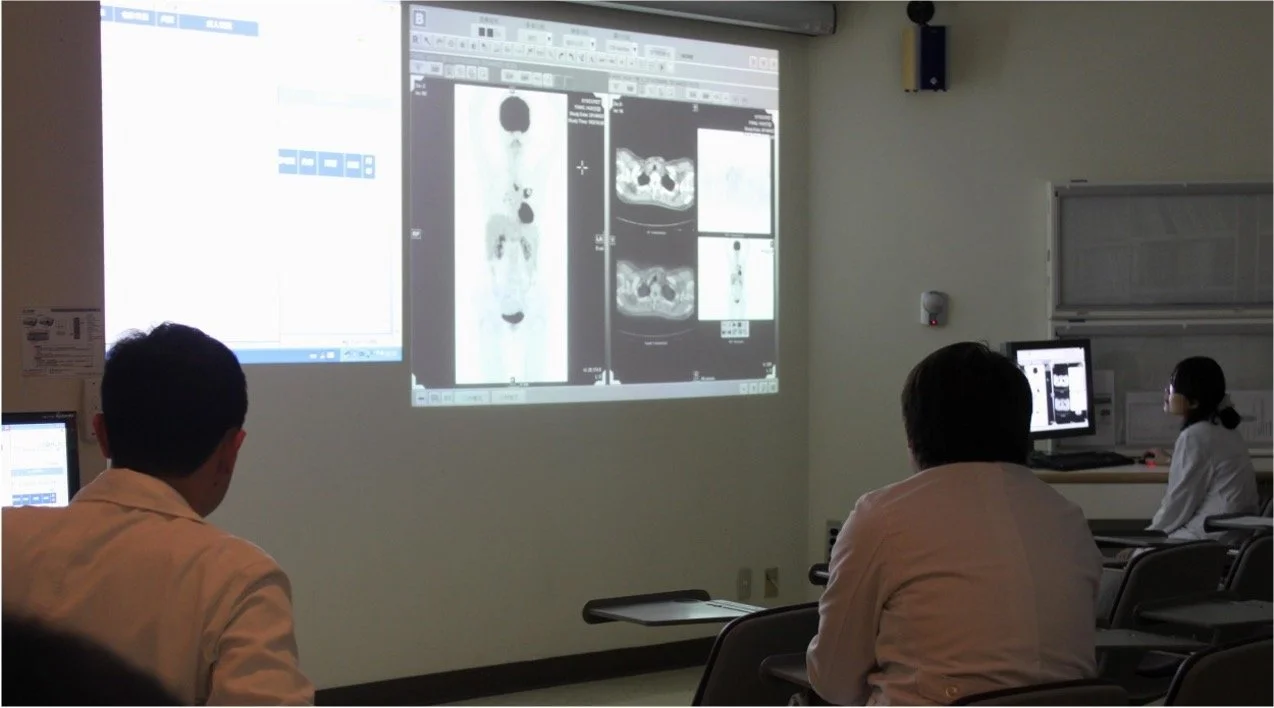 Medical professionals observing radiology images of spinal scans projected on a large wall screen in a medical conference room.