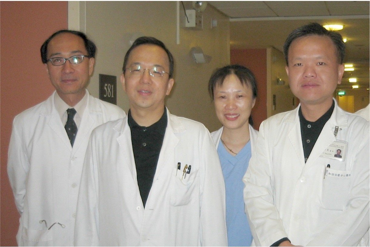 Group of four medical professionals, three men and one woman, standing in a hospital corridor, wearing white coats.