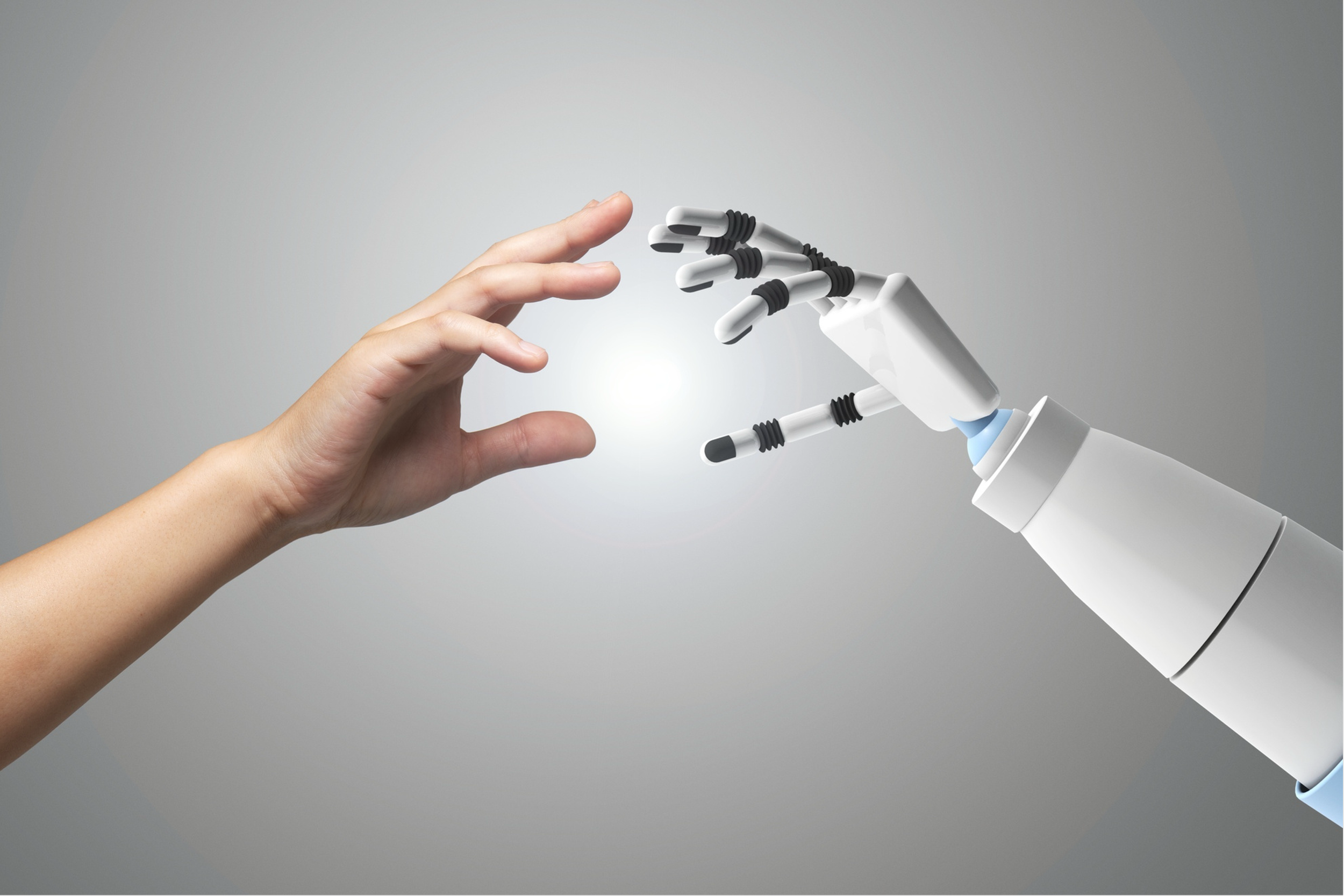 A human hand reaching out to a robotic hand with a glimmering light in between, symbolizing connection between humans and robots.