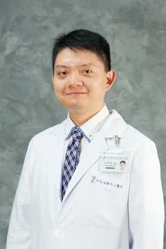 Portrait of a man in a white lab coat with a name badge, standing against a gray background.