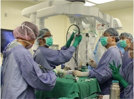 Surgeons operating in a sterile environment in an operating room with advanced medical equipment, including a C-arm fluoroscopy device and surgical tools.