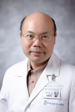 Portrait of a male doctor wearing glasses and a white lab coat, with a name badge, against a gray background.