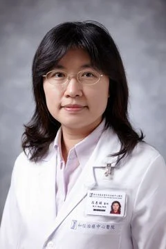 Professional woman with glasses in a white medical coat, posing against a gray background.