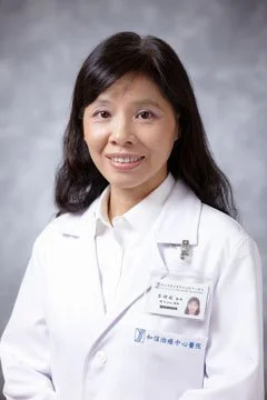 A woman in a white lab coat smiling for a professional portrait against a gray background.