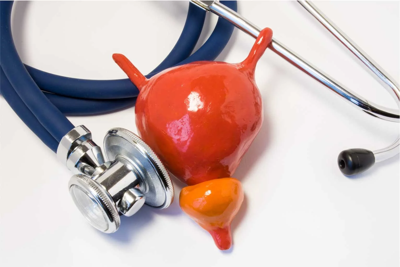 A stethoscope, a large red ceramic heart, and a smaller orange ceramic heart on a white surface.