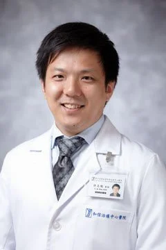 A male doctor in a white lab coat smiling at the camera against a gray background.