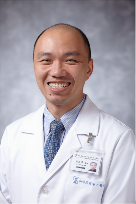 A smiling male doctor wearing a white lab coat, a striped shirt, and a patterned tie, with an ID badge on his coat.