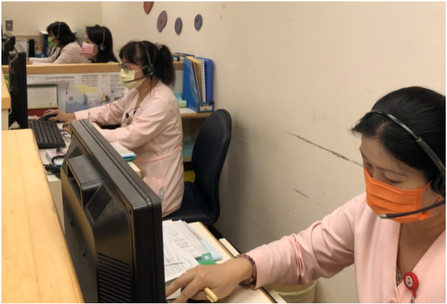 Nurses wearing masks and headsets working at desks with computers, documents, and medical supplies in a healthcare setting.