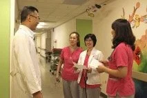 Three women and one man in a hospital hallway, with the women holding clipboards and the man wearing a white lab coat.