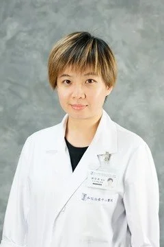 Portrait of a woman in a white medical coat against a gray background.