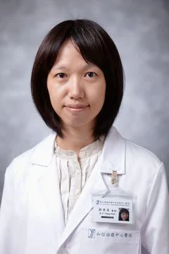 Woman in white medical coat and identification badge against gray background.
