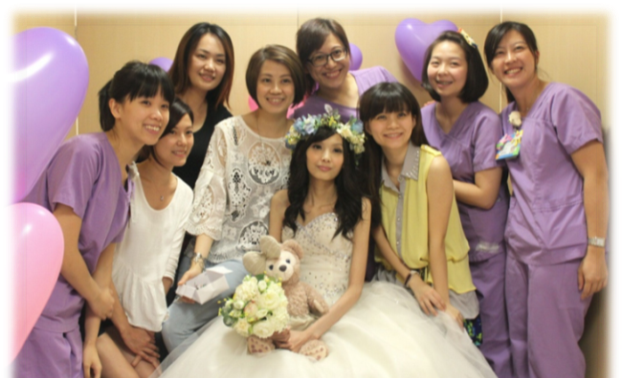 Group of women dressed in purple and white, celebrating a young woman in a wedding dress with a floral crown, surrounded by pink and purple balloons.