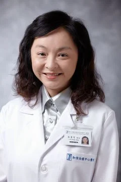 A smiling woman in a white medical coat with an ID badge.