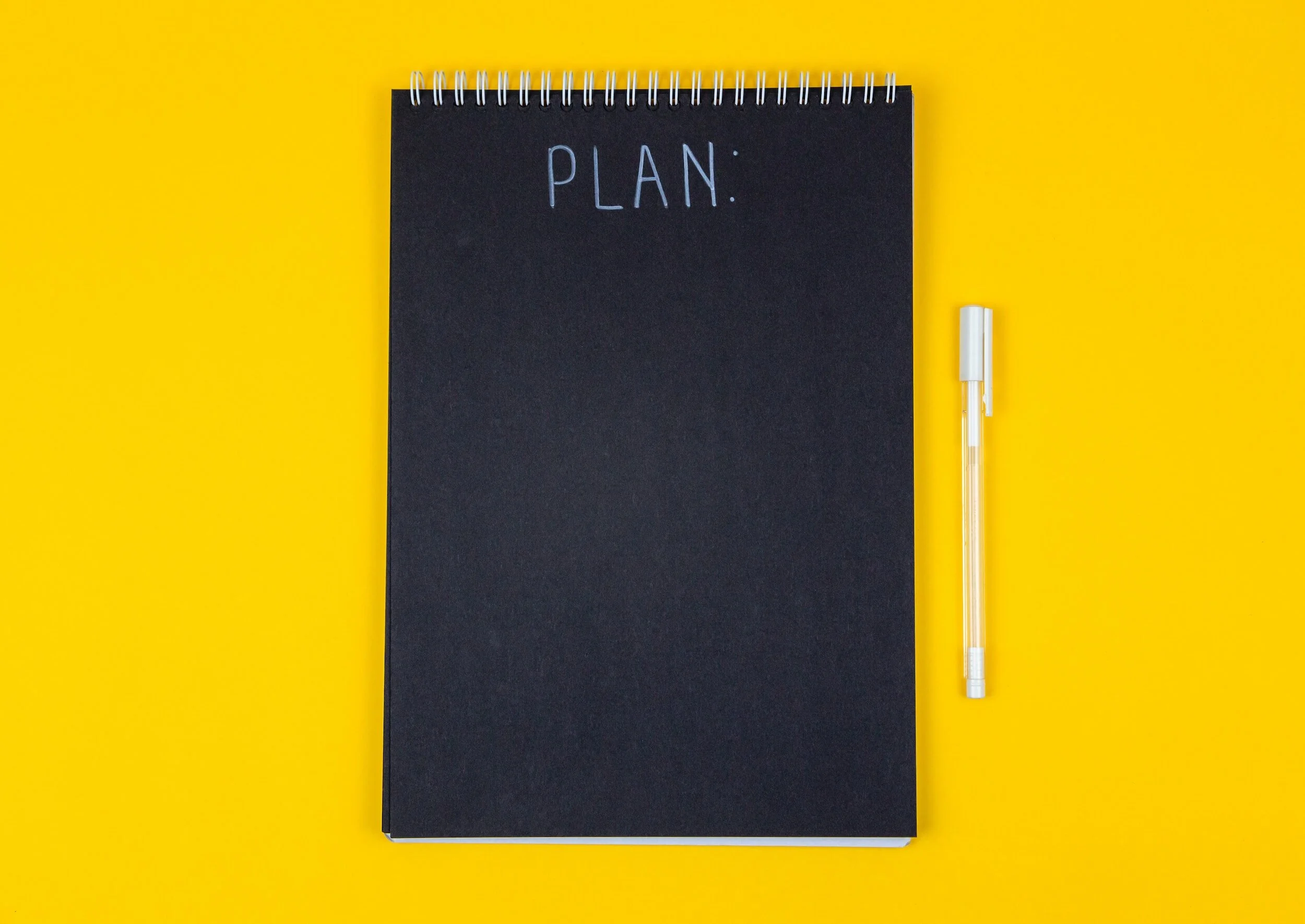 Black notebook labeled 'Plan' with a pen on a yellow background.