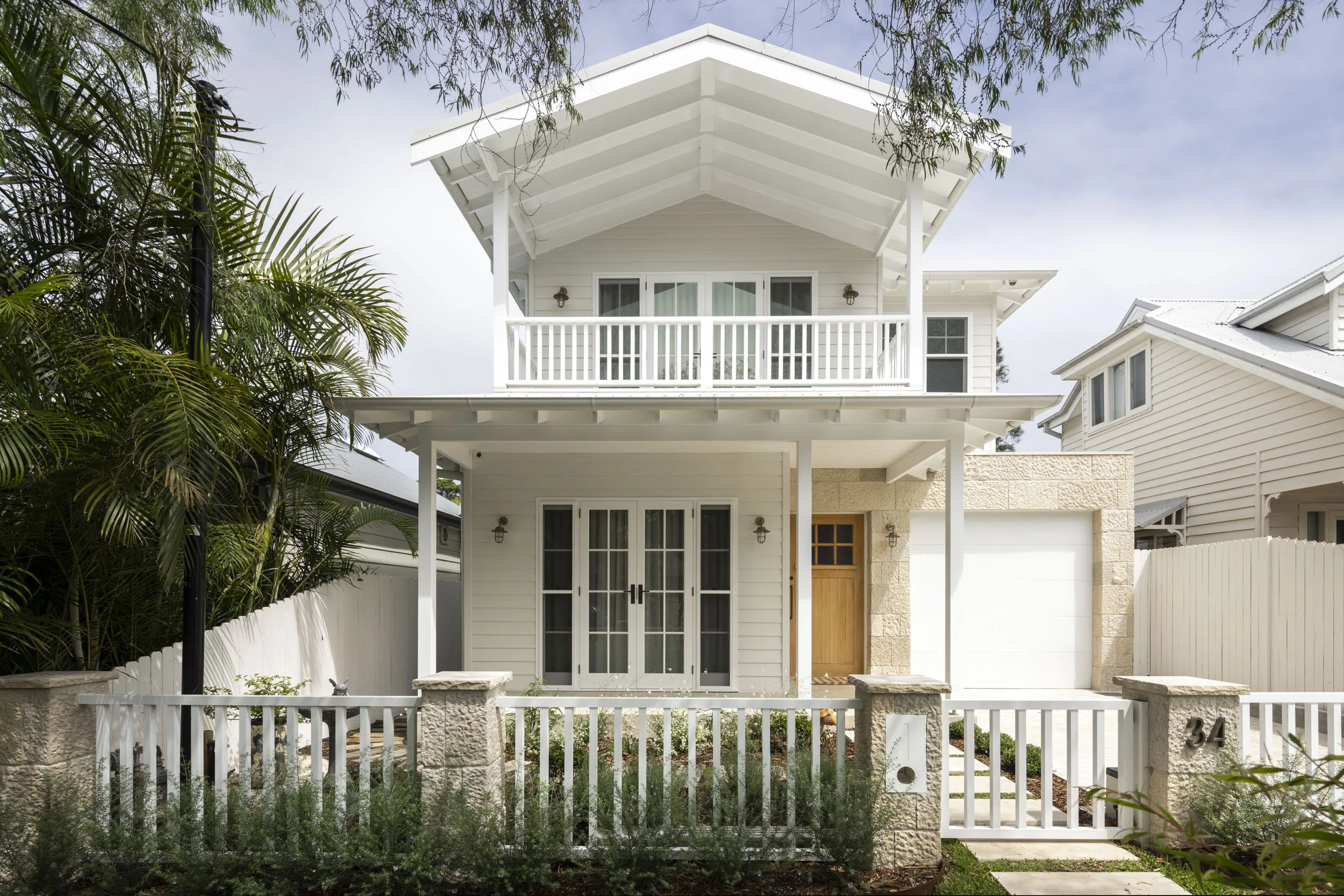 Front view of a modern two-story house with a white exterior, black roof, and a black front door, featuring a covered porch, potted plants, and garage with small window panels.