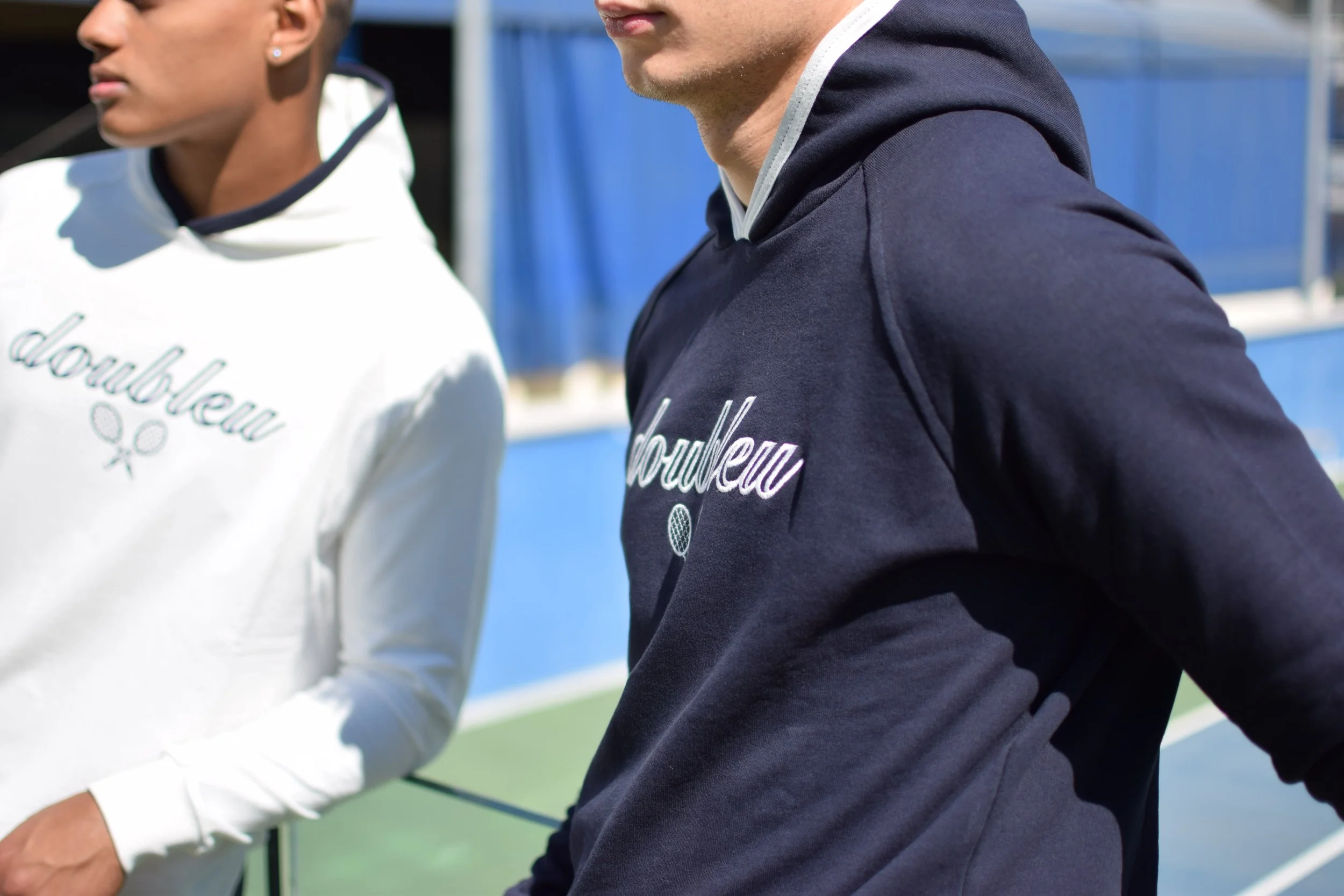 Due persone con felpe con il logo 'Doubleu' in un campo da tennis all'aperto.