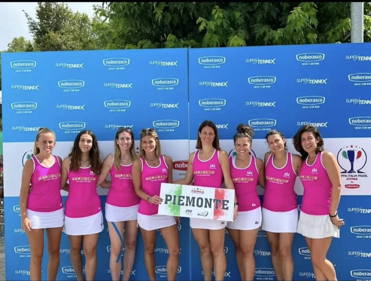 Gruppo di otto donne festanti in uniforme rosa e bianca, che tengono un cartello con la scritta "PIEMONTE", davanti a uno sfondo blu con loghi di sponsorizzazione e di sport.