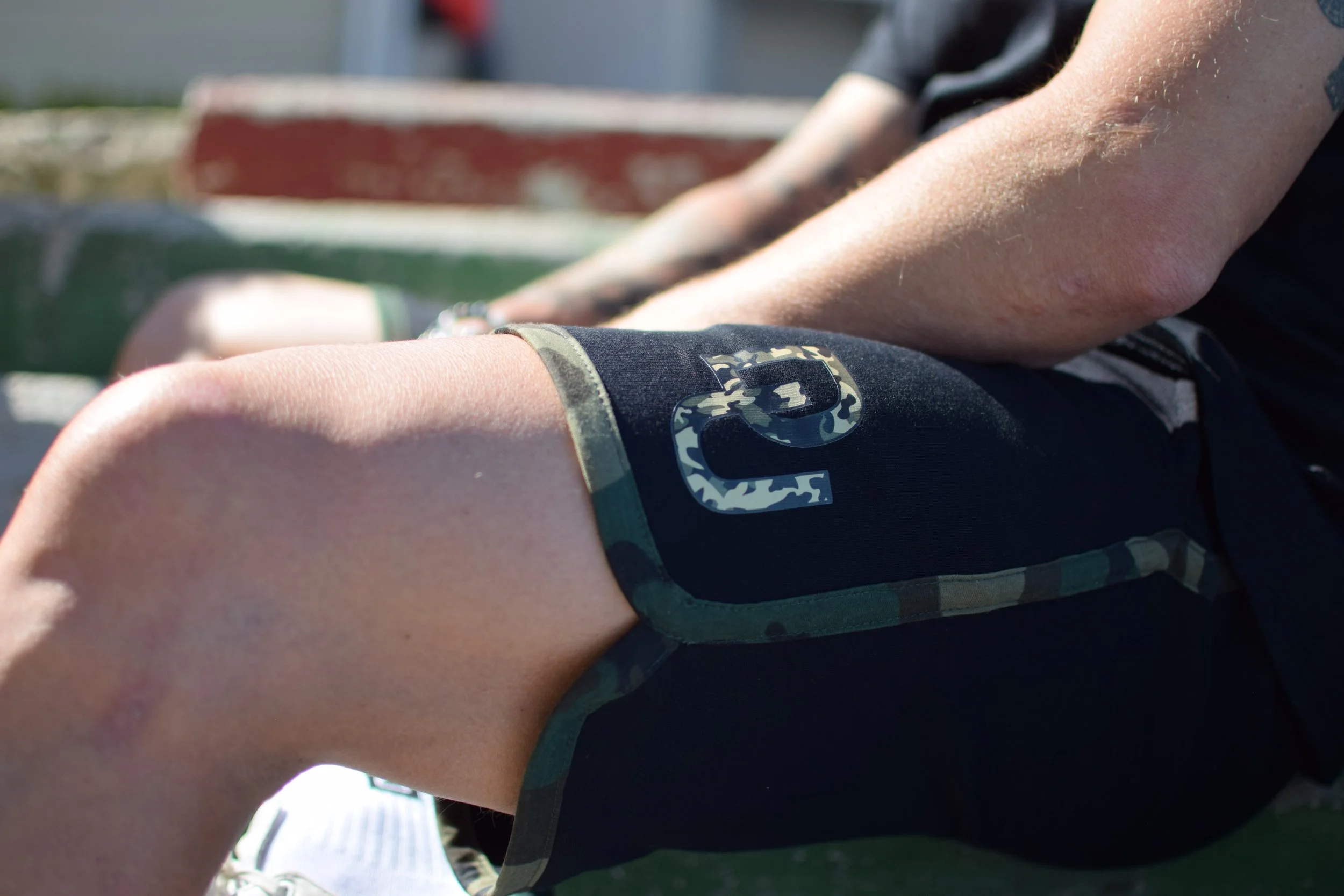 Gamba di un atleta, indossando pantaloncini neri con dettagli camouflage, seduto su una panchina.