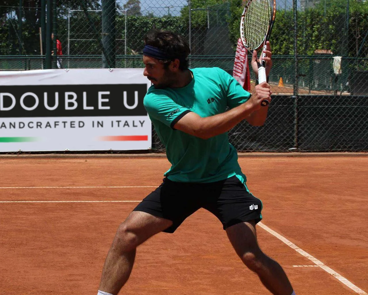 Giocatore di tennis in azione sul campo in terracotta, pronto a colpire la palla con la racchetta.