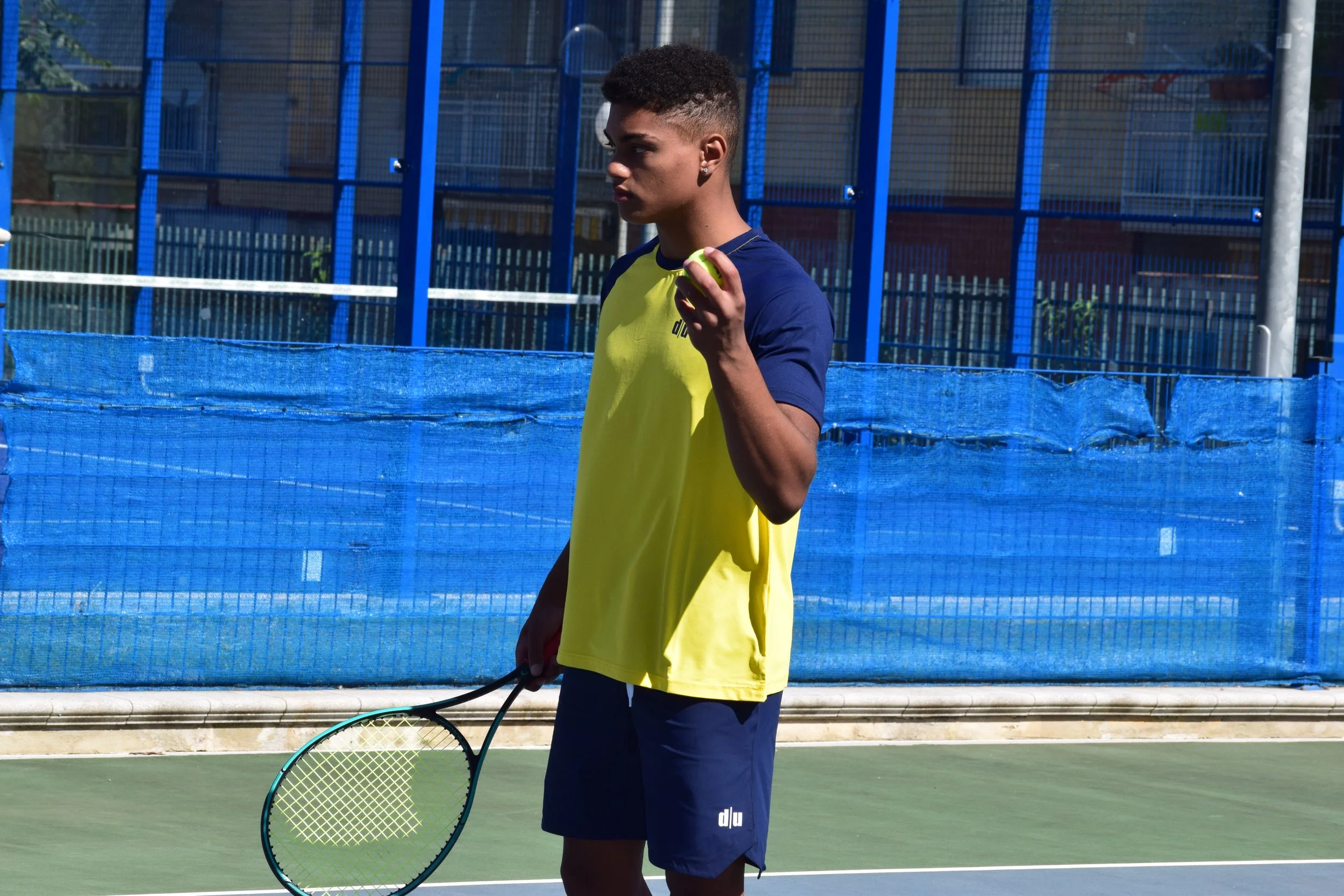 Una giovane persona tiene una racchetta da tennis in una mano e una pallina da tennis nell'altra, sul campo da tennis all'aperto.