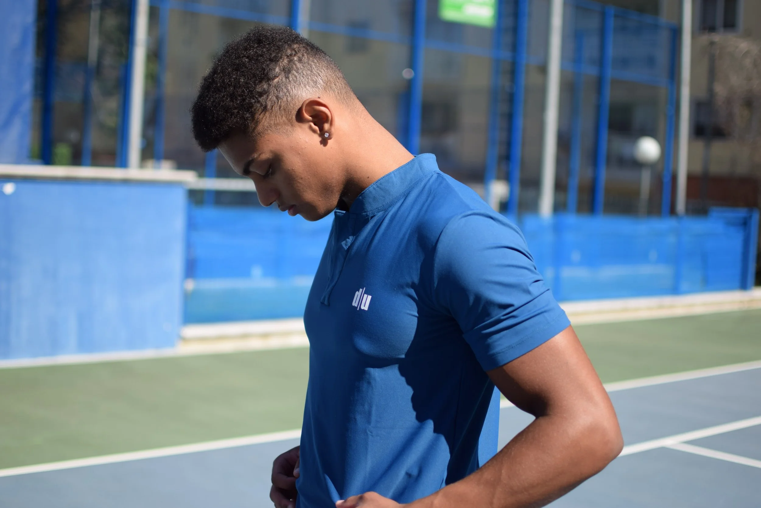 Giovane atleta che si sistema la maglietta su un campo da tennis all'aperto.
