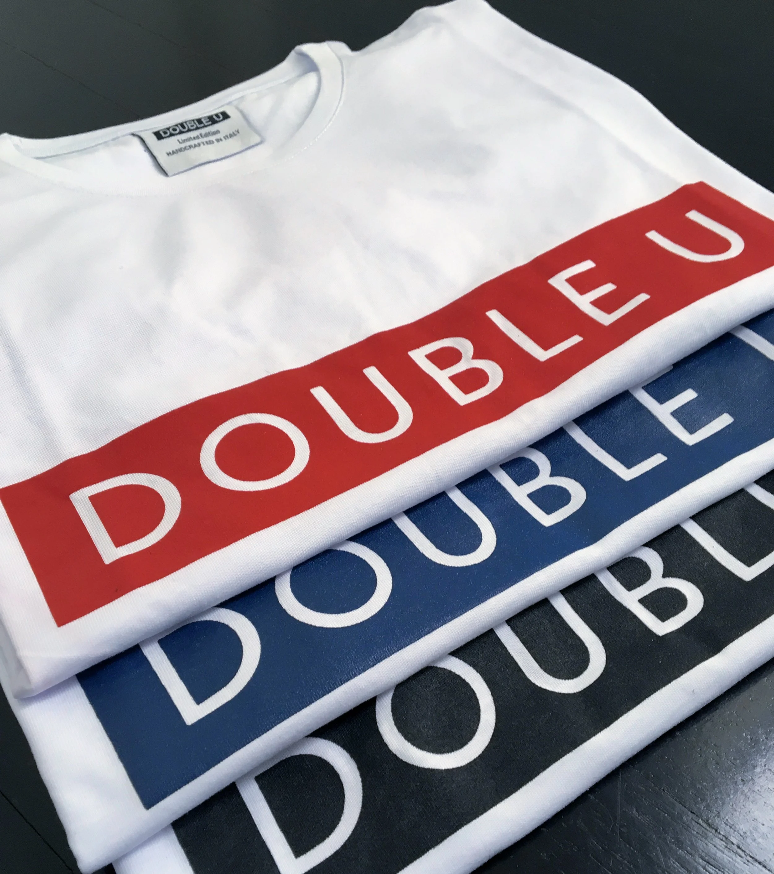 Magliette bianche con la scritta 'DOUBLE U' in diversi colori: rosso, blu e nero