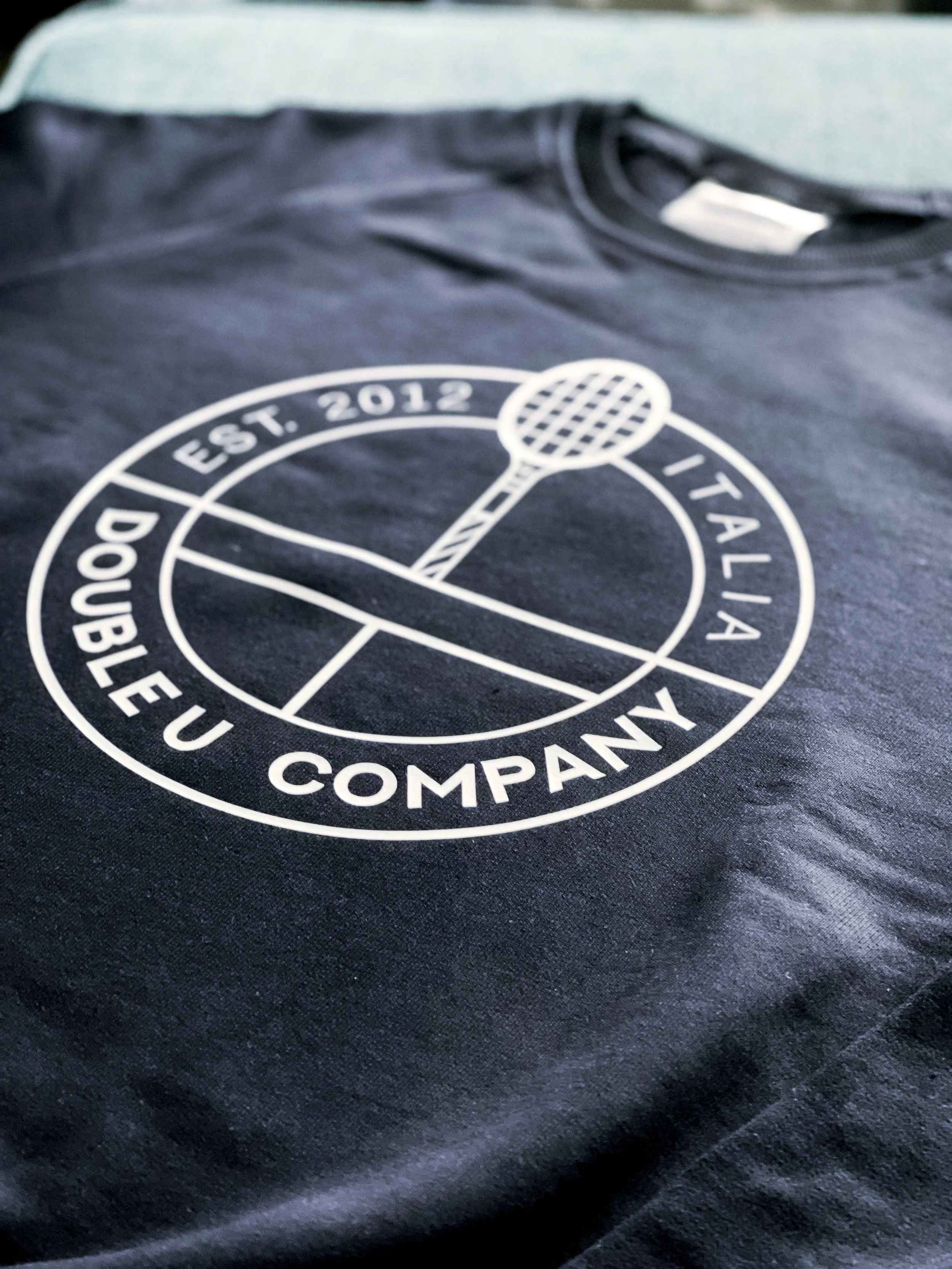 Maglietta nera con logo circolare bianco e immagine di una racchetta da tennis, scritto 'DoubLe Eu Company, Est. 2012, Italia'.