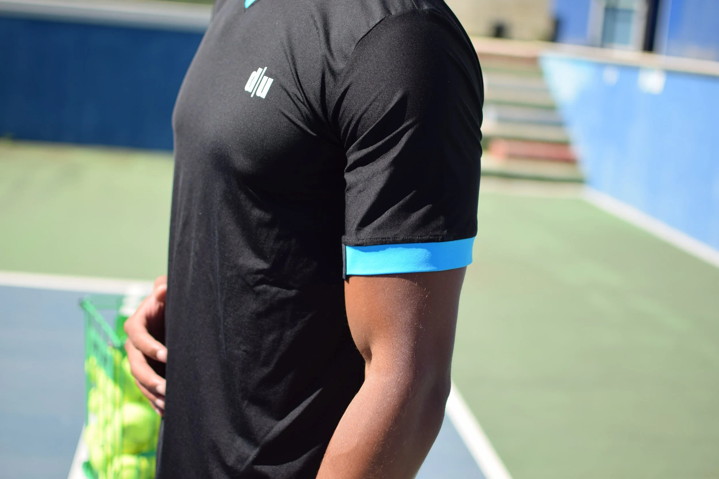 Persona che indossa una maglietta da calcio nera con dettagli azzurri, su un campo da tennis.