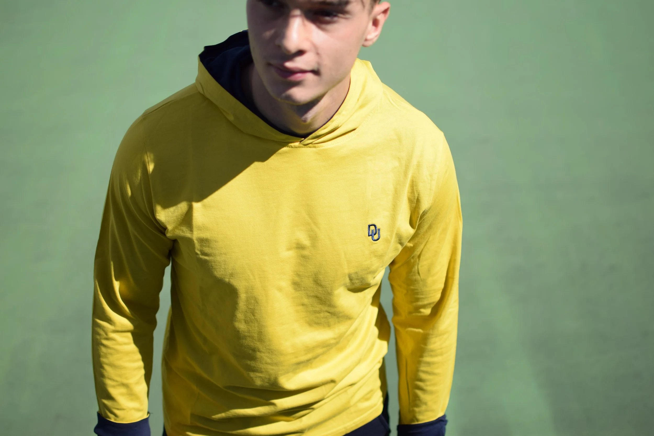 Ragazzo in maglietta gialla con logo di Oklahoma University sul petto, in piedi su campo di calcio.