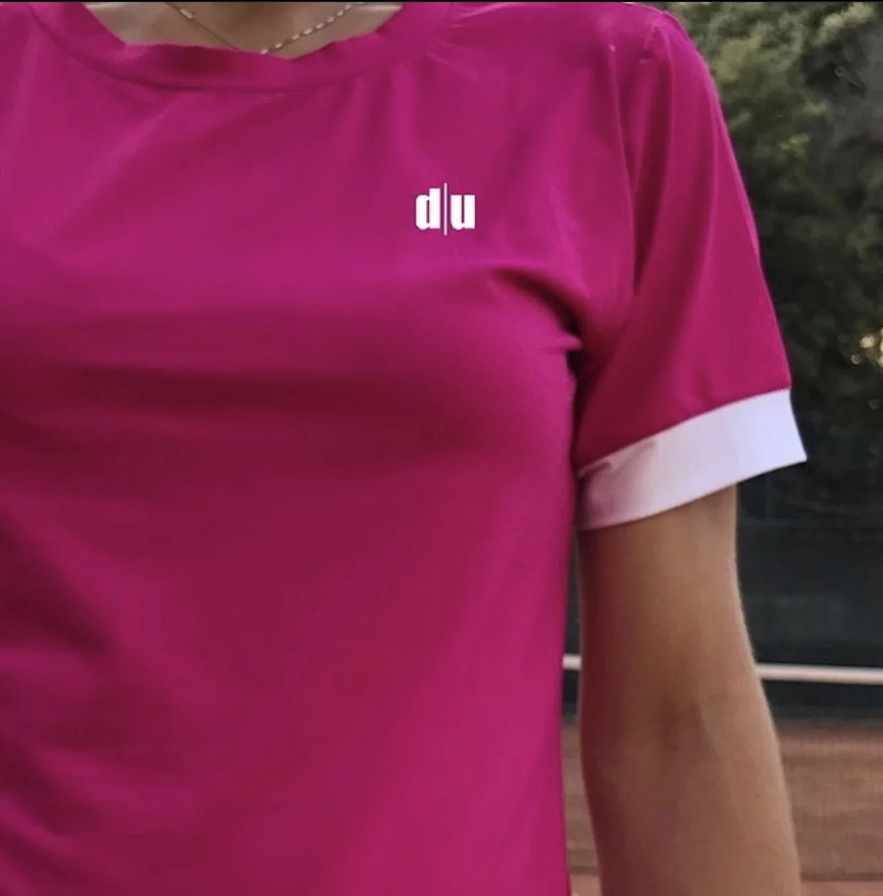 Un braccio di una persona con maglietta rosa con risvolto bianco sulla manica e una collana d'argento.