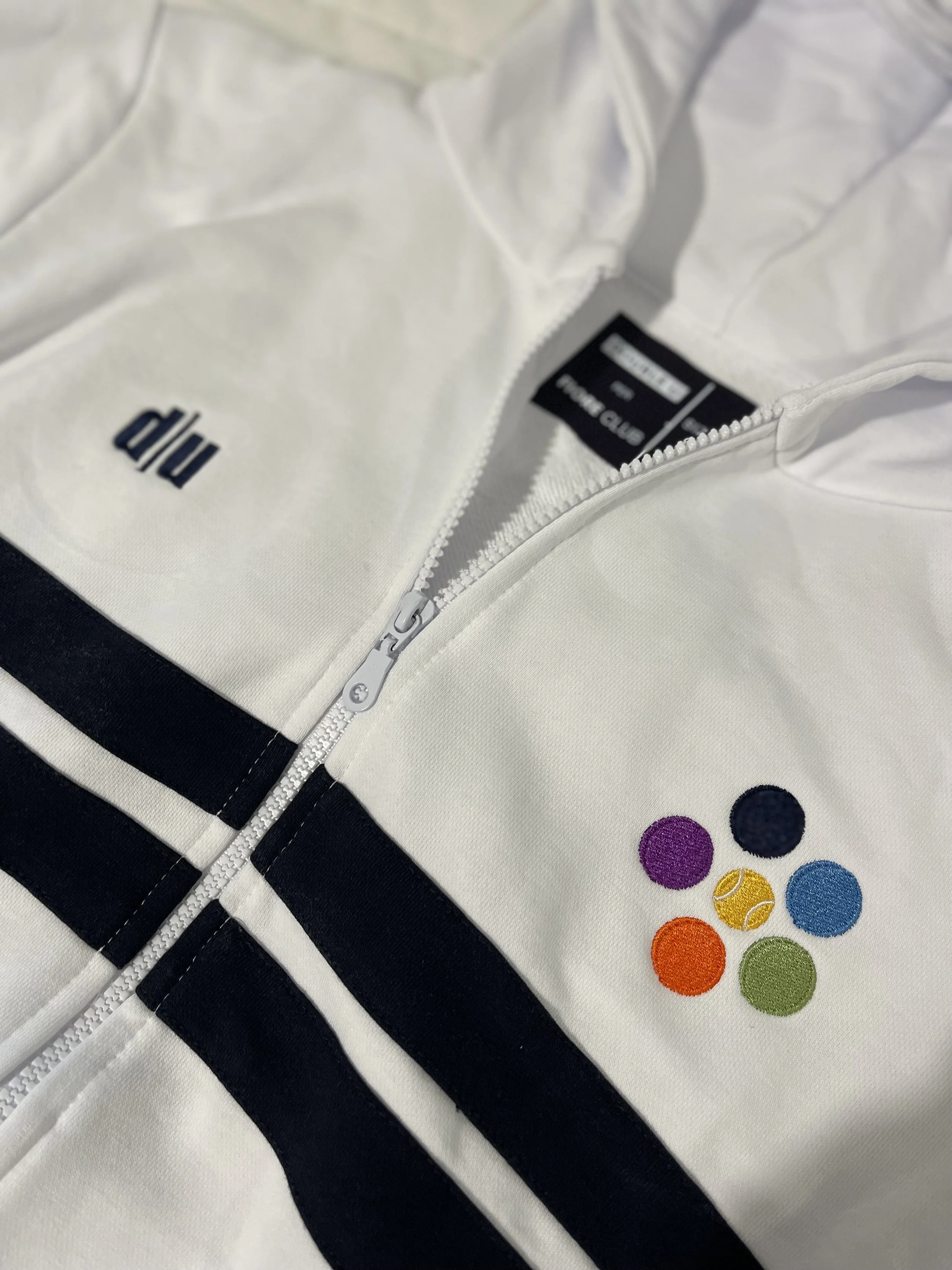 Giacca bianca con zip, logo 'dhu' e cinque punti colorati ricamati.