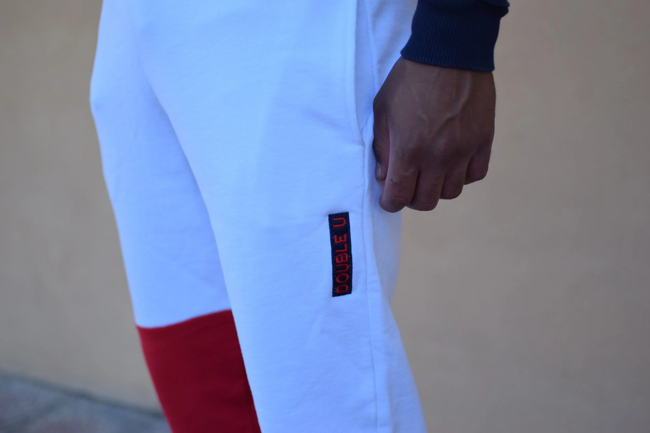 Gamba di una persona vestita con pantaloni bianchi con dettagli rossi e una etichetta con la scritta 'DOUBLE U'.