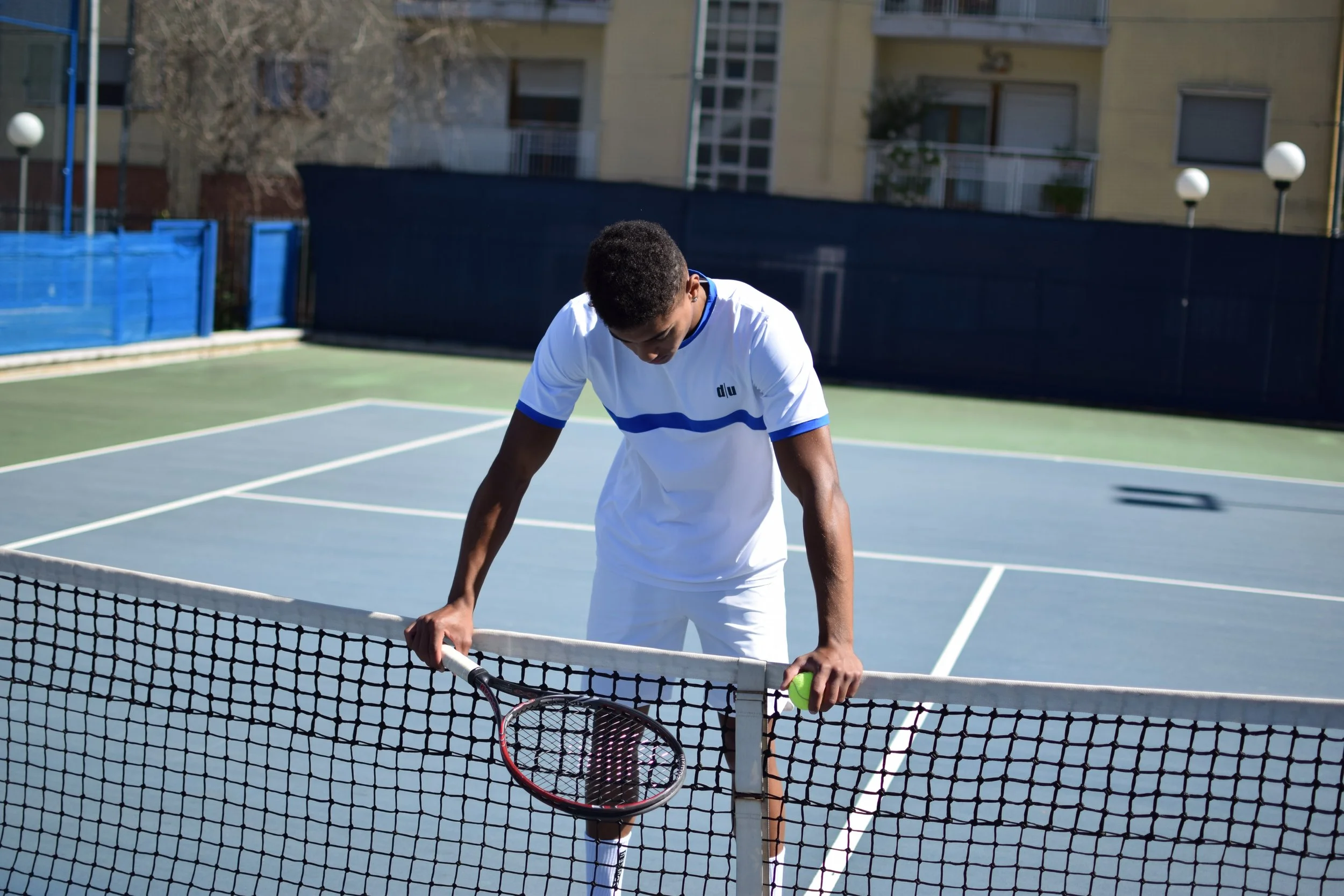 Giovane uomo su un campo da tennis, chinato con racchetta e pallina in mano, dopo aver giocato.