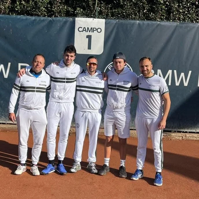 Cinque uomini vestiti con divise sportive bianche che si abbracciano davanti a un cartellone che dice 'Campo 1'.