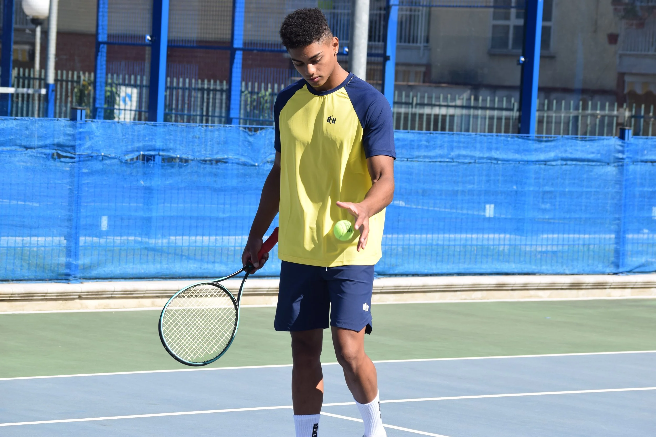 Giovane ragazzo in campo da tennis con racchetta e palla, abbigliamento sportivo, durante il gioco all'aperto.