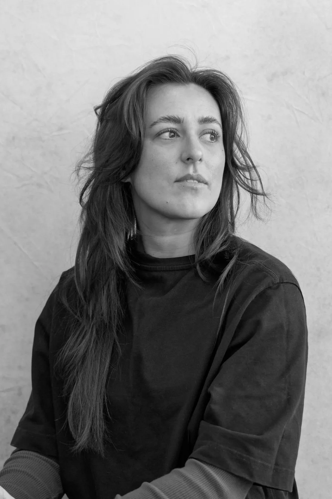 Black and white portrait of a woman with wavy hair, looking to her left, wearing a casual dark top.