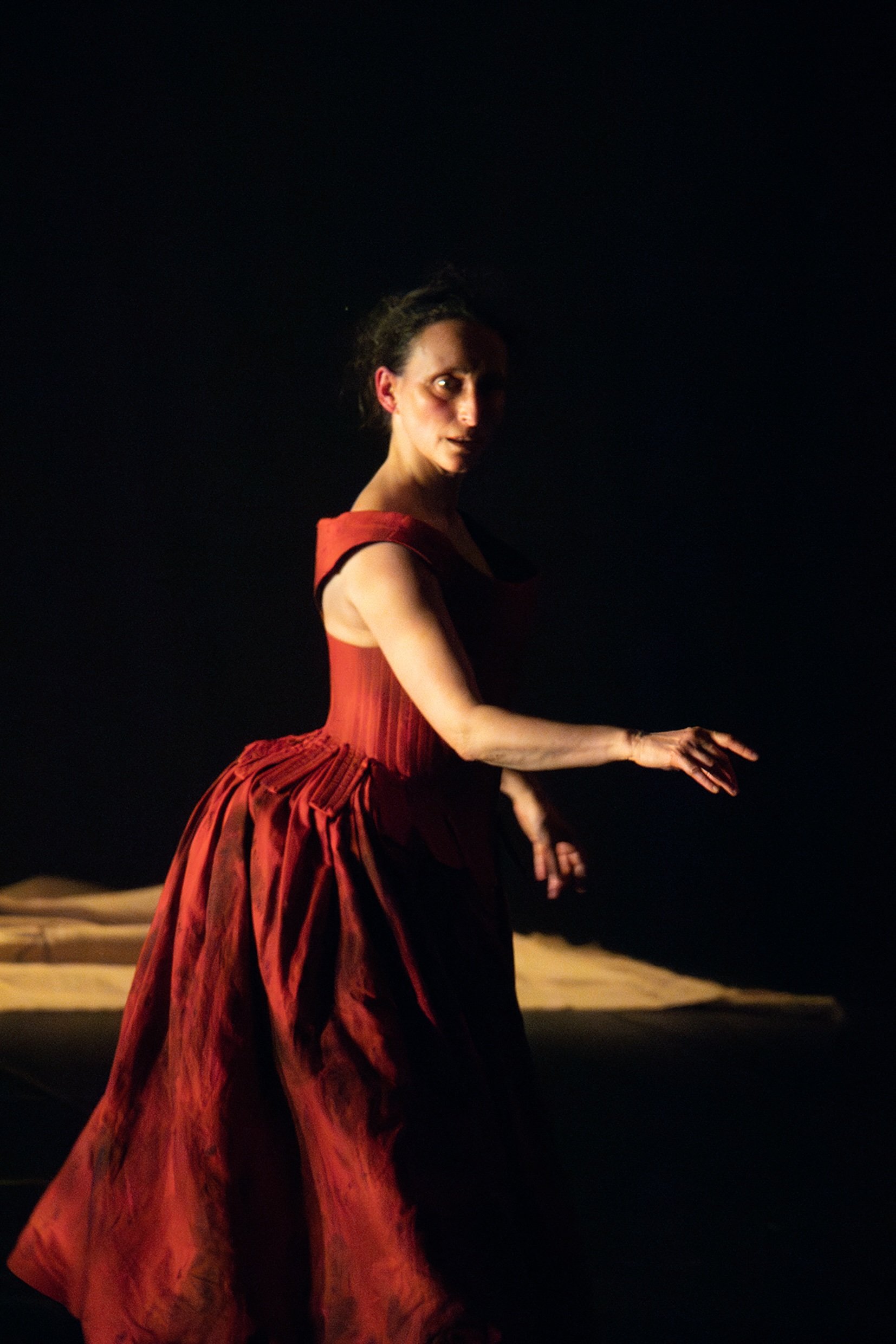 A woman in a red dress performing on stage with a dark background.