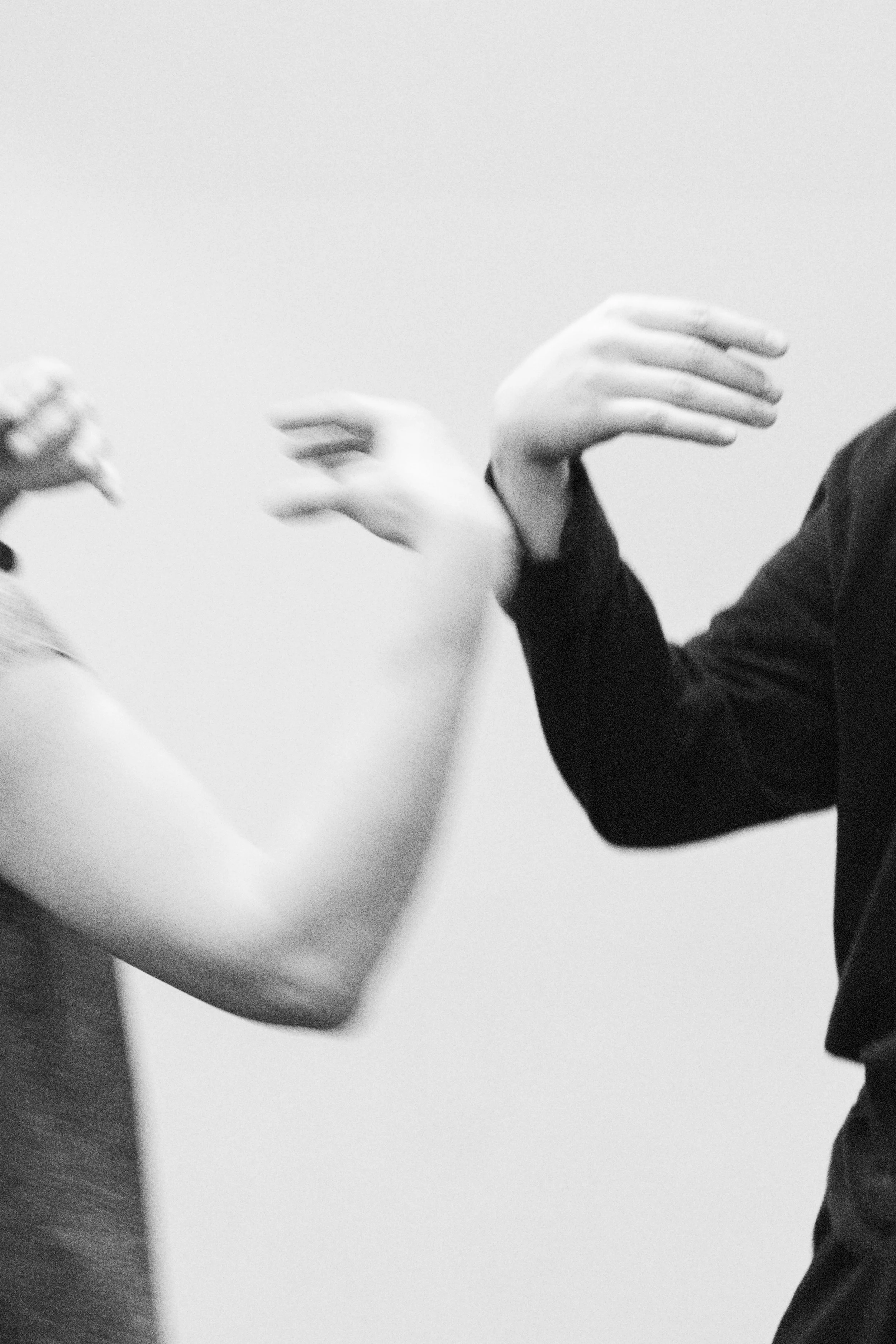 Black and white photo of two people arm wrestling, focusing on their flexed arms and hands, with one person's hand visible on the left and the other's on the right.