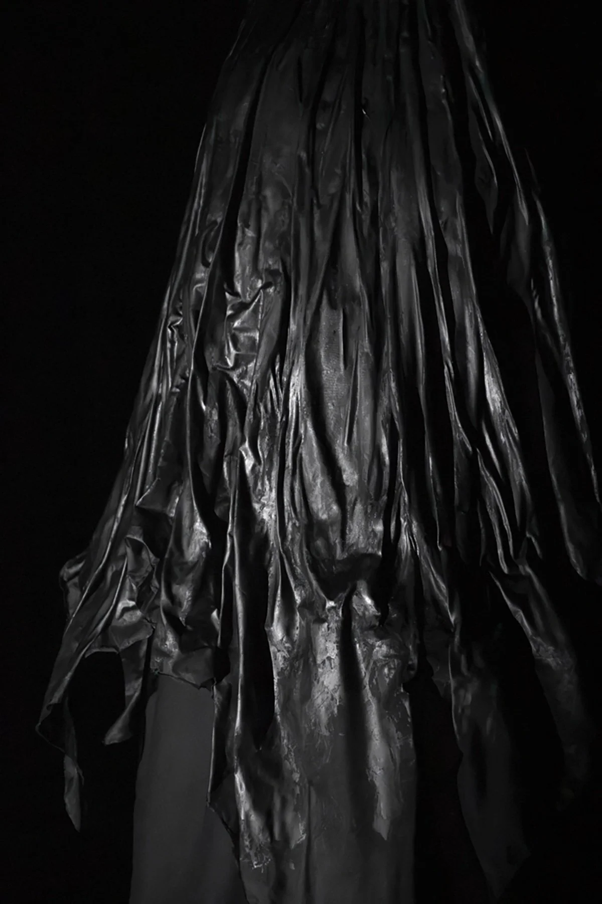 Close-up of a black, crinkled plastic sheet hanging against a dark background.